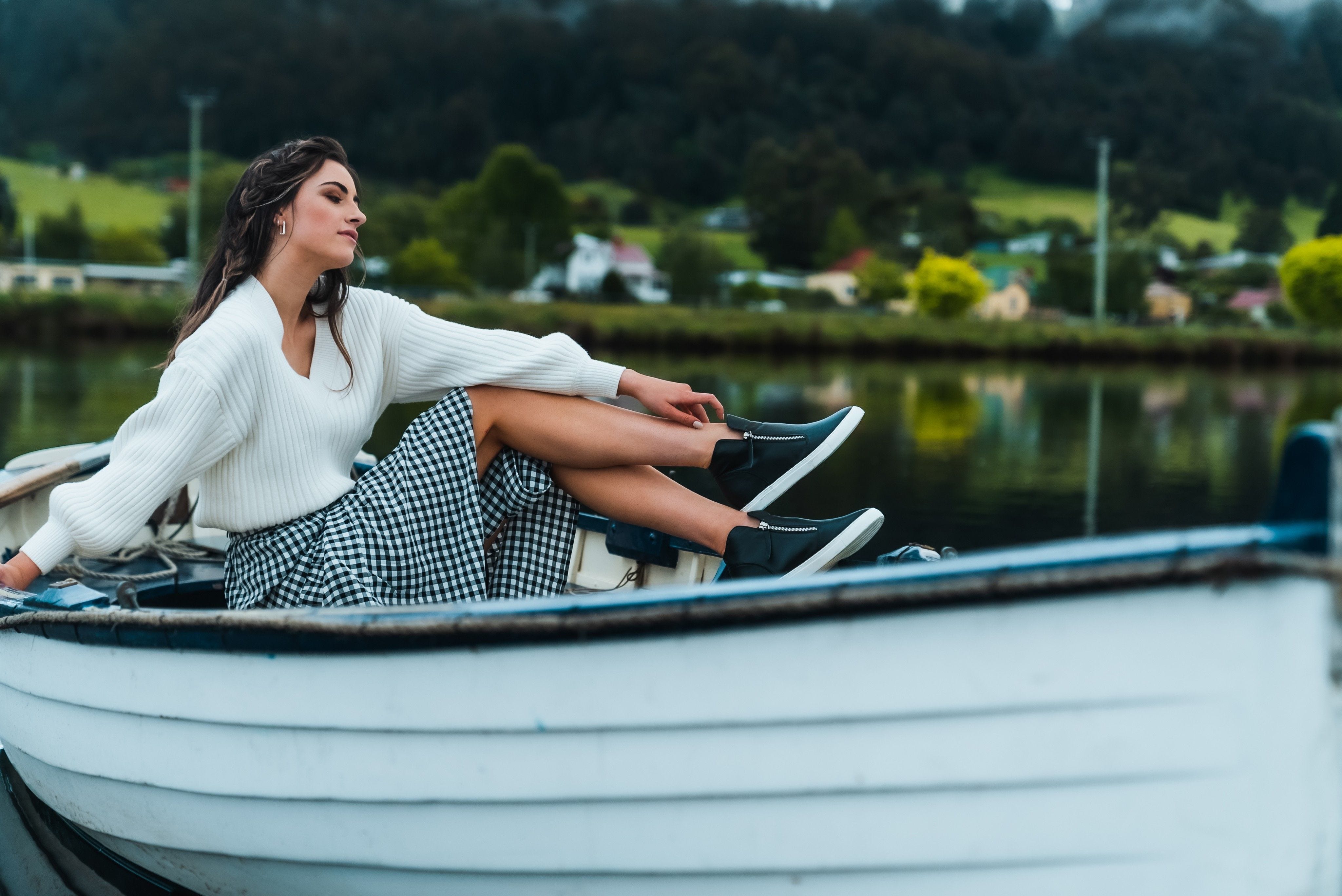 A young woman wearing leather shoes with zips sitting in a small boat on a country side lake.